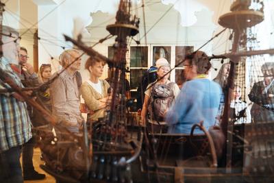 Blick durch die Vitrine mit einem Schiffsmodell auf Gäste in der Wunderkammer
